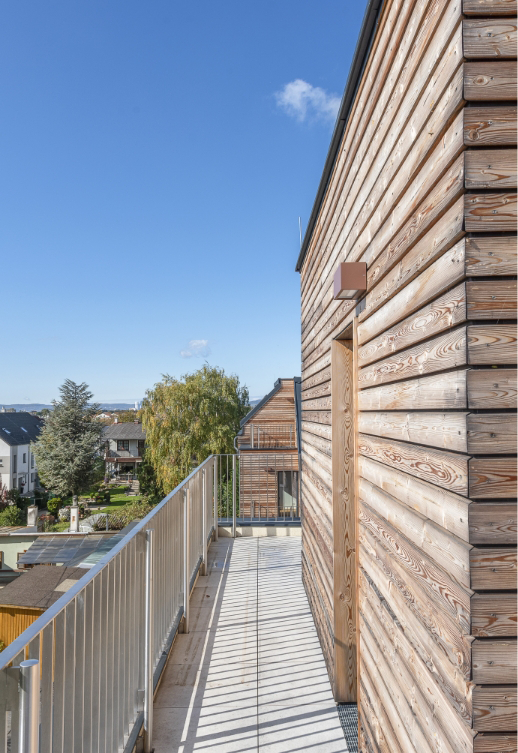 Langer Balkon mit Metallgeländer und Holzfassade, mit Blick in die Umgebung.