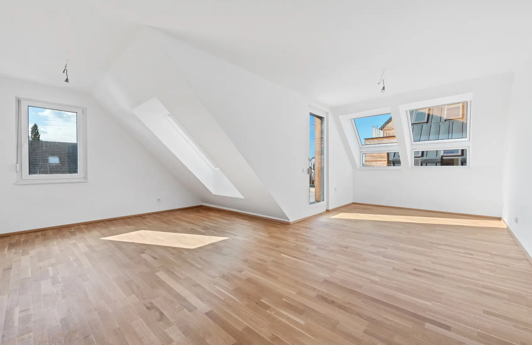 Heller, leerer Dachgeschossraum mit Parkettboden und verschiedenen Dachfenstern.