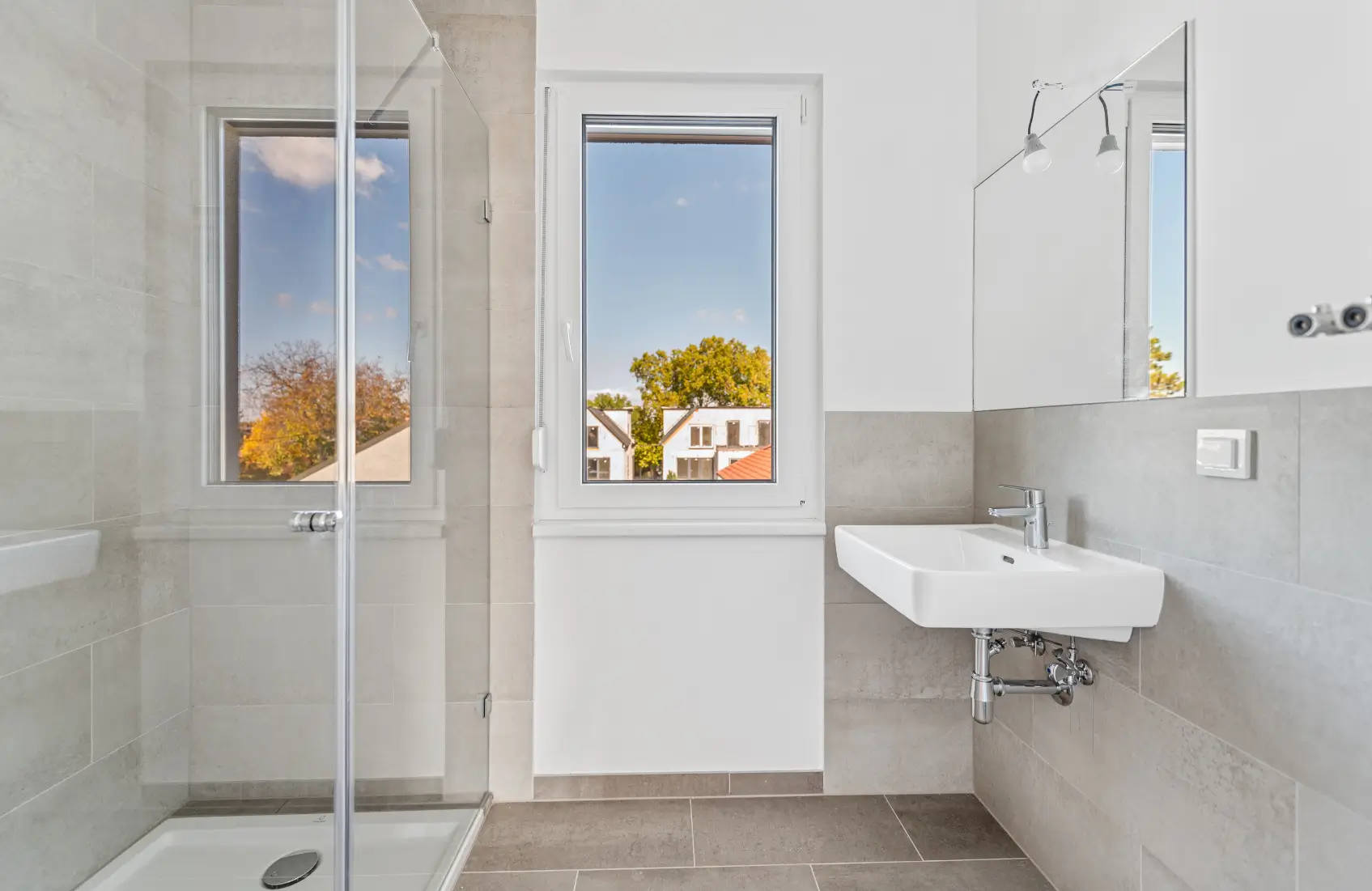 Modernes Badezimmer mit Dusche, Waschbecken und zwei Fenstern mit Blick nach draußen.