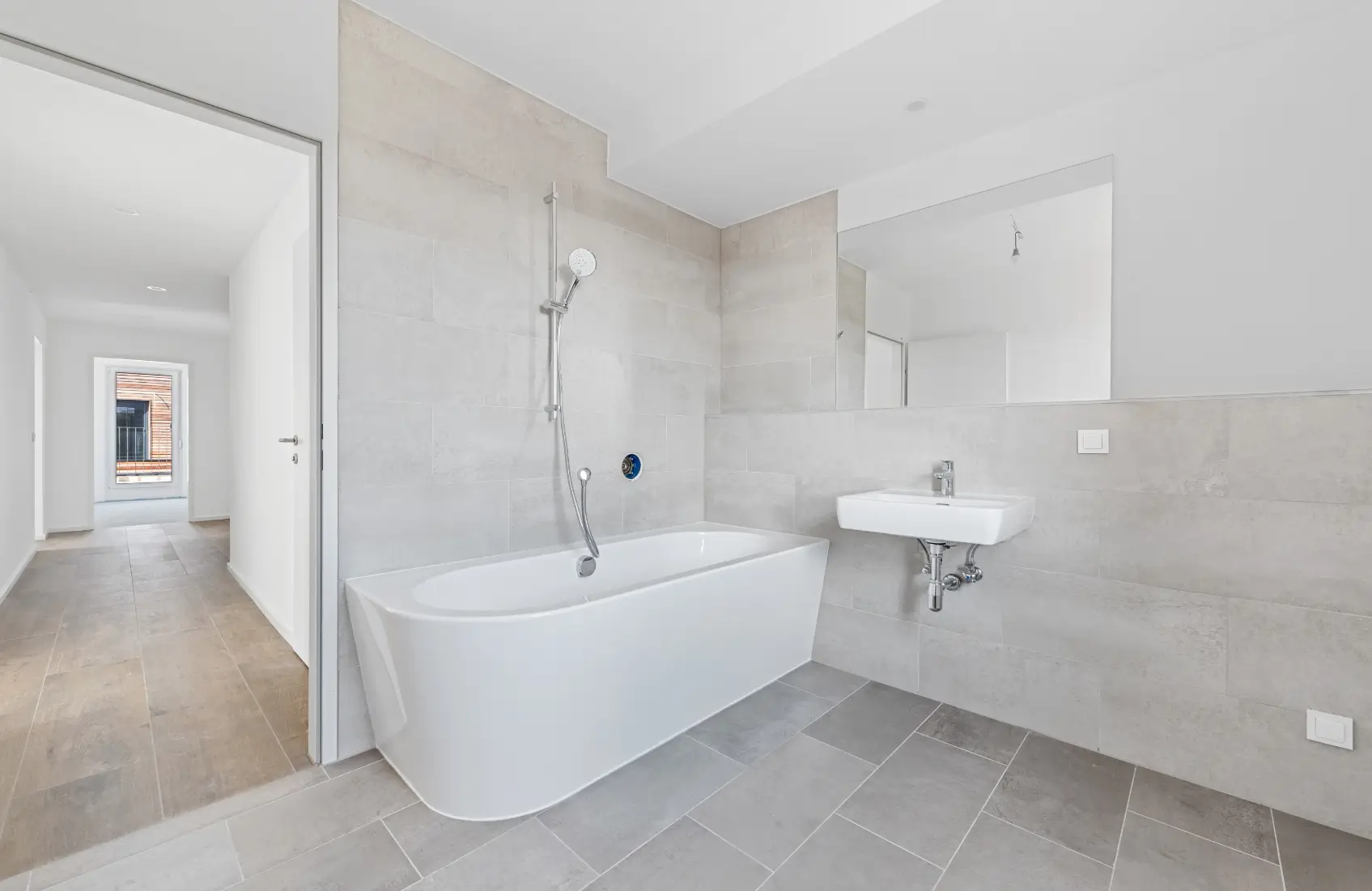 Modernes Badezimmer mit freistehender Badewanne und Waschbecken, im Hintergrund ein Flur.