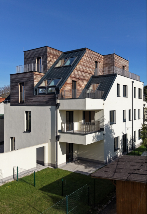 Modernes Wohnhaus mit weißer Fassade und Holz-Dachaufbauten, umgeben von einem kleinen Garten.