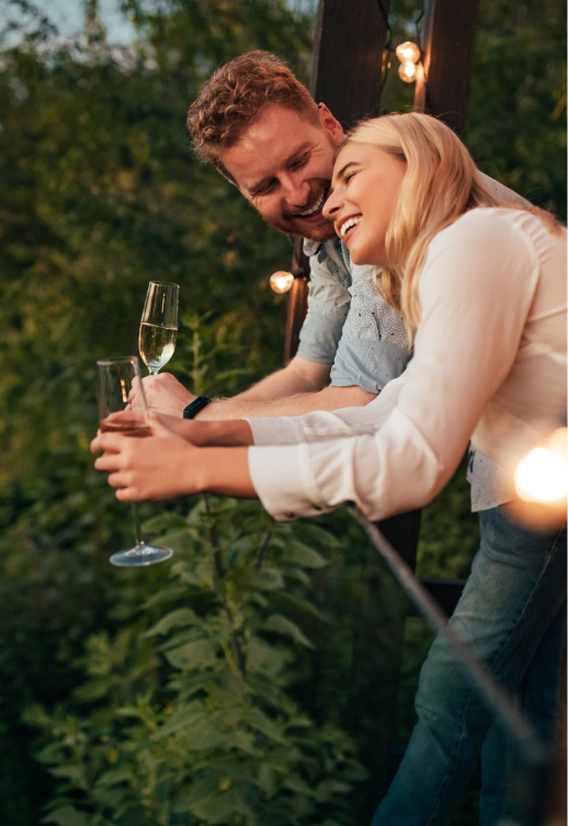 Lächelndes Paar trinkt Sekt auf einem Balkon oder einer Terrasse im Freien.